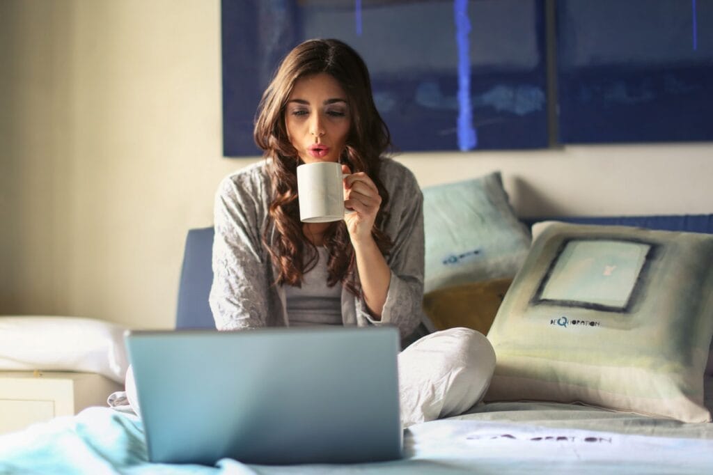 Kvinde i grå drikker kaffe og kigger på computer